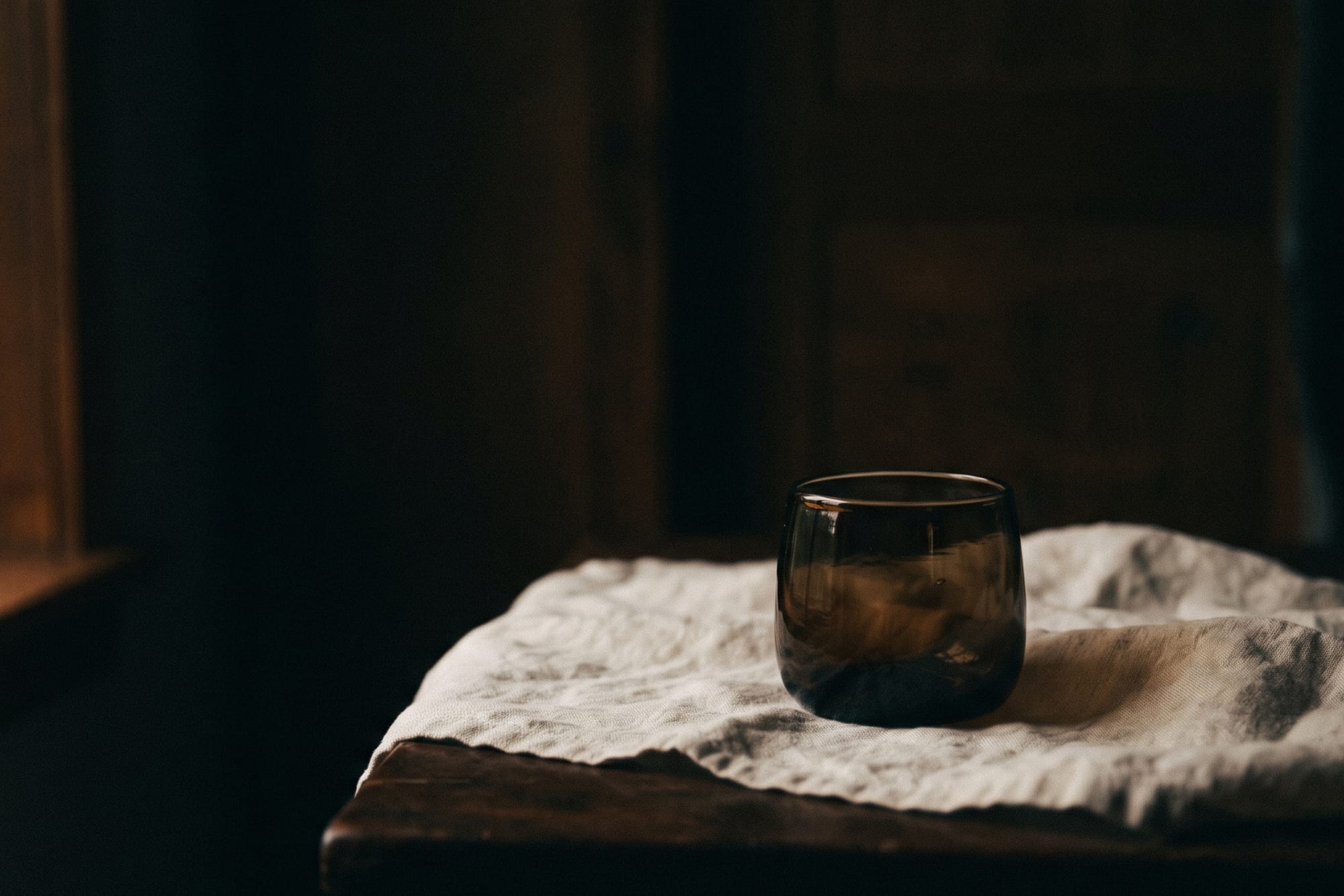 깊고 따뜻한 어둠 속, 리넨 위에 쉬는 브라운-블랙 유리 용기 — 회복의 밤